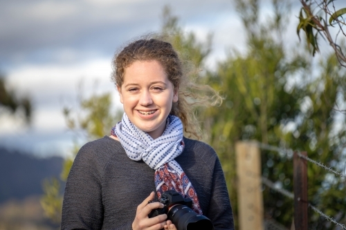 Young girl holding a camera smiling at the camera - Australian Stock Image