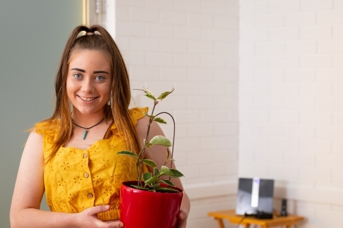 Young girl holding a plant in a red pot - Australian Stock Image