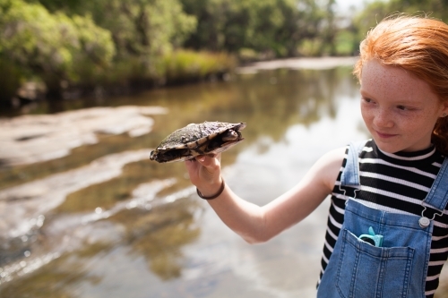 Young girl holding a turtle by the river - Australian Stock Image