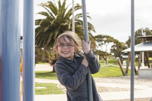 Young girl holding onto pole at playground - Australian Stock Image