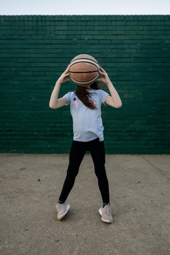 Young girl holding up a basketball in front of her face - Australian Stock Image
