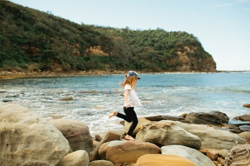 Young girl hopping across rocks at the beach - Australian Stock Image