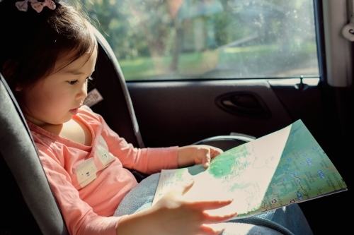 Young girl in car seat reading map on road trip - Australian Stock Image