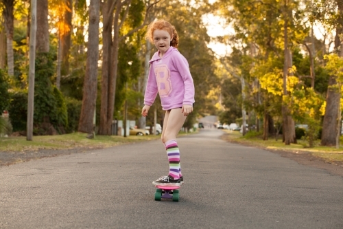 Young girl in long socks riding a skateboard along a road - Australian Stock Image