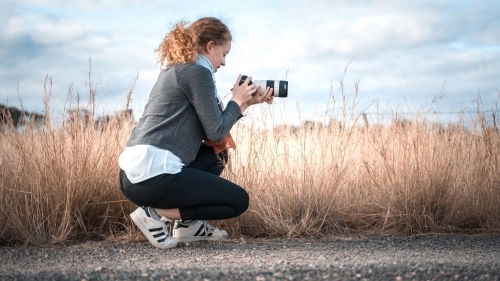 Young girl in profile kneeling taking picture of landscape
