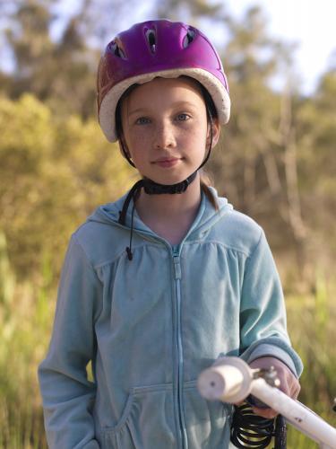 Young girl in purple helmet preparing to go bike riding - Australian Stock Image
