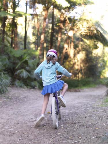 Young girl in purple helmet riding bike on bush track - Australian Stock Image