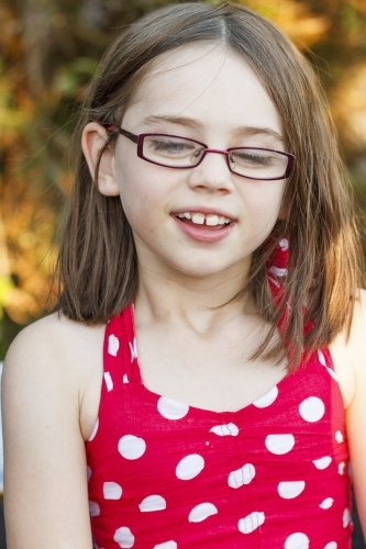 Young girl in red polka dot dress looking down - Australian Stock Image