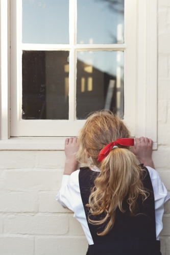 Young girl in school uniform peeking through a window - Australian Stock Image