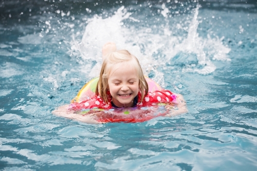 Young girl in swimming pool using a swimming ring, splashing with eyes closed - Australian Stock Image