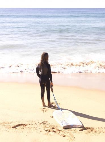 Young girl in wetsuit on beach entering water with body board