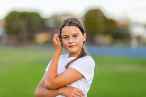 young girl in white tee outdoors looking at camera with hand to face - Australian Stock Image