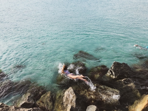 Young girl jumping into ocean from rocks