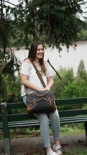 Young girl leaning on park bench with bag - Australian Stock Image