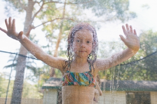 Young girl looking through the net of a trampoline