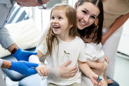Young girl looking up to the doctor wrapping her arm with white bandage - Australian Stock Image