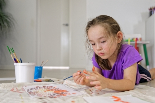 Young girl lying on the floor putting colour on her finger for painting a dot picture - Australian Stock Image