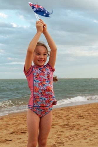 Young girl of mixed race standing and playing on the beach on Australia Day waving small flags