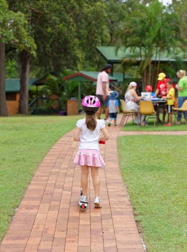 Young girl on scooter wearing helmet watching people playing - Australian Stock Image