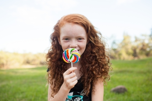 Young girl outside eating a rainbow lollipop