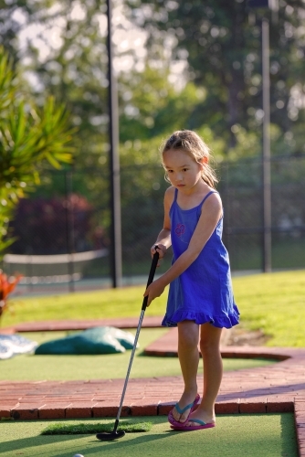 Young girl playing mini golf or putt-put holding golf iron - Australian Stock Image
