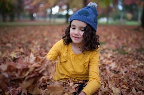 Young girl playing outdoors among piles of autumn leaves - Australian Stock Image