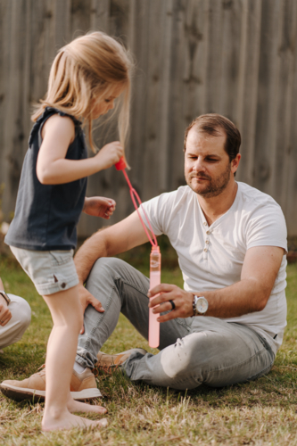 Young girl playing with bubbles inside their yard. - Australian Stock Image