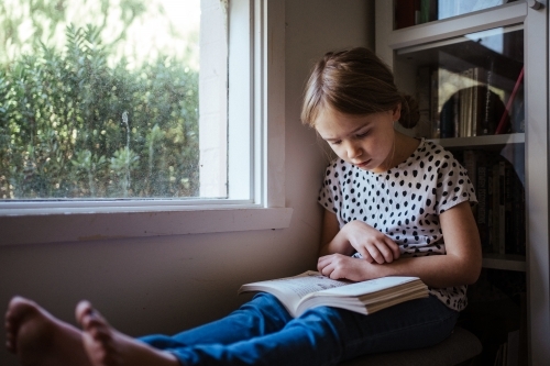 Young girl reading a book at home - Australian Stock Image