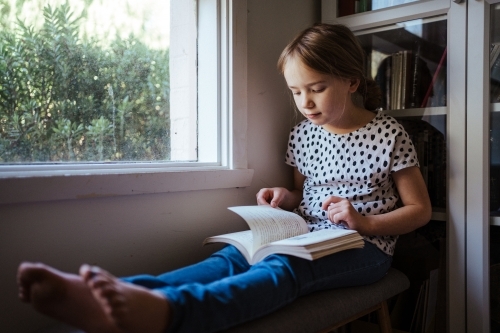 Young girl reading a book at home - Australian Stock Image