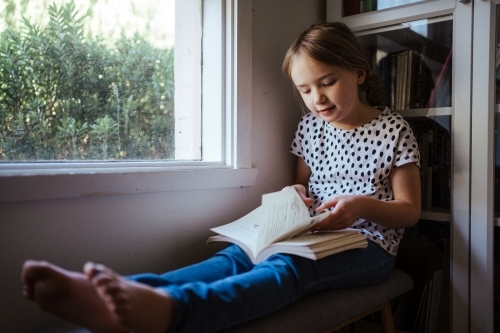 Young girl reading a book at home - Australian Stock Image