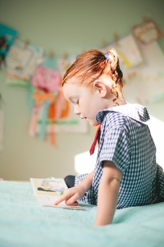 Young girl reading a book in a bedroom - Australian Stock Image