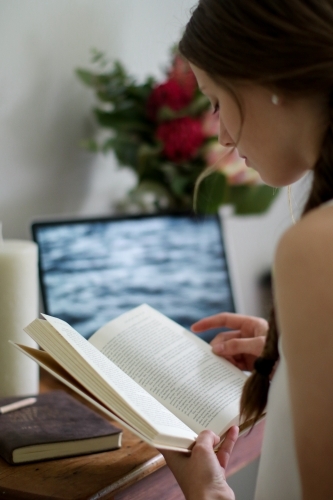 Young girl reading a book indoors by her work desk - Australian Stock Image
