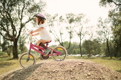 Young girl riding a bike over a hill in backyard