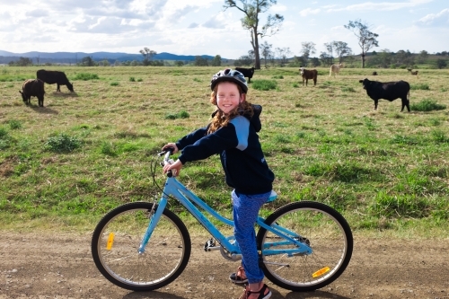 Young girl riding a bike through a cow paddock - Australian Stock Image