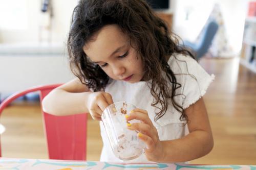 Young girl scooping out chocolate from bottom of glass - Australian Stock Image