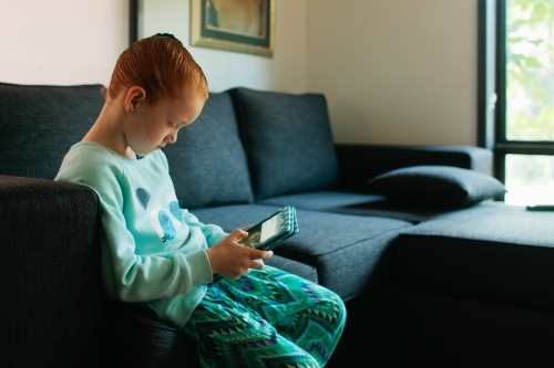Young girl sitting on a lounge reading a tablet - Australian Stock Image