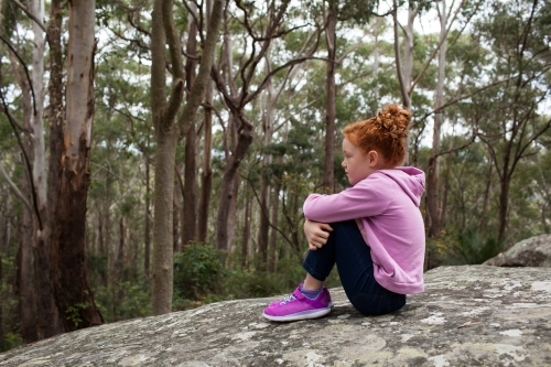 Young girl sitting on a rock with knees bent - Australian Stock Image