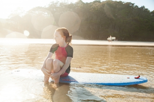 Young girl sitting on a surfboard at the beach - Australian Stock Image
