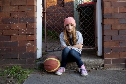 Young girl sitting on sidewalk with basketball