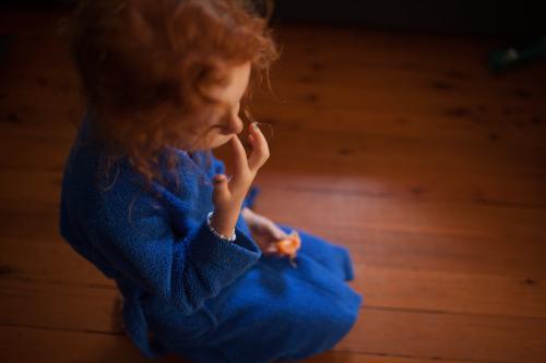 Young girl sitting on the floor eating a mandarin - Australian Stock Image