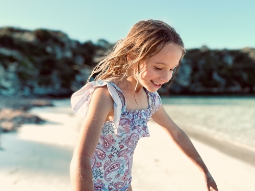 Young girl smiling in pastel swimsuit standing on beach with salty long wet hair