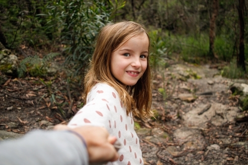Young girl smiling in the wilderness holding parents hand on an adventure - Australian Stock Image
