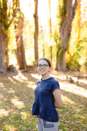 Young girl smiling with autumn trees behind her - Australian Stock Image
