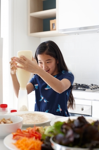 Young girl squeezing out mayonnaise whilst preparing healthy lunch in kitchen - Australian Stock Image