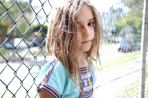 Young girl standing against chain link fence - Australian Stock Image