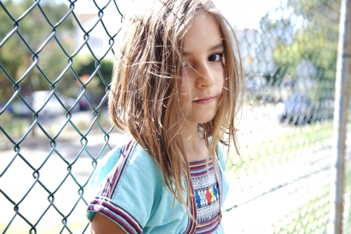 Young girl standing against fence looking at camera