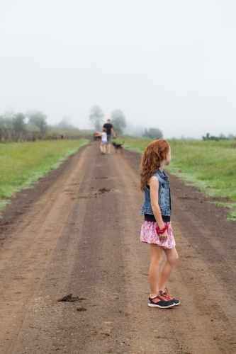 Young girl standing on a dirt track with family in the distance - Australian Stock Image