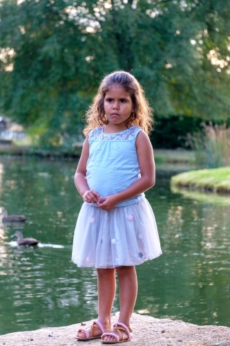 Young girl standing on a flat rock on the lakeside. - Australian Stock Image