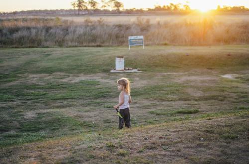Young girl standing on rural golf course at sunset - Australian Stock Image
