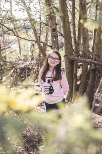 Young girl standing with arms behind back in some trees - Australian Stock Image